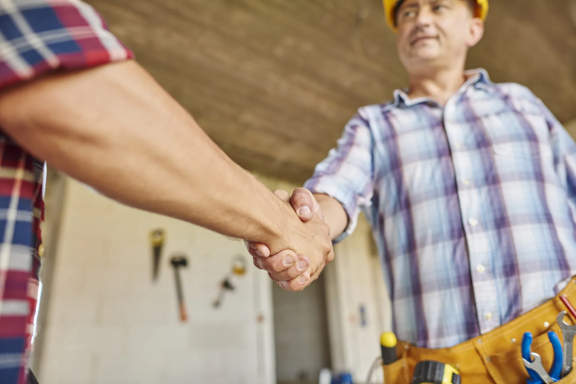 Two tradies shaking hands on a residential job site with tools nearby.