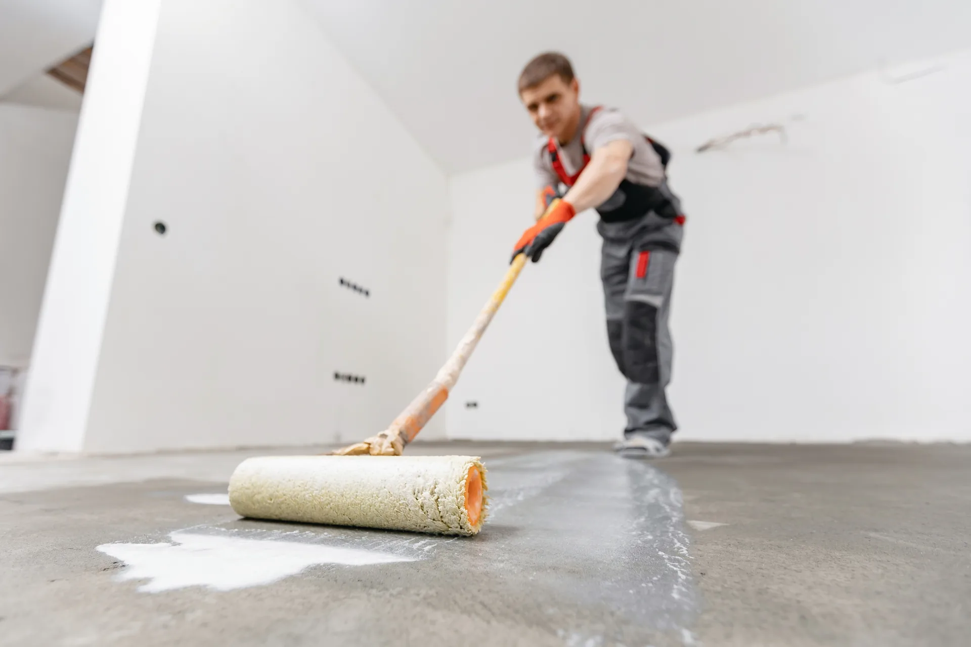Tradesperson rolling primer onto a bare concrete floor.