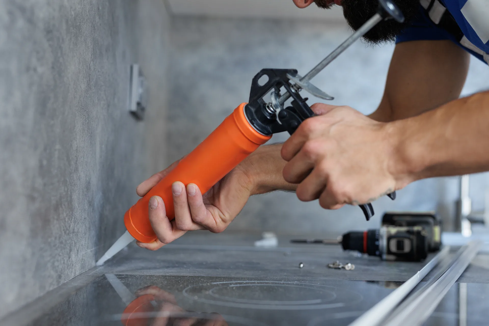 Orange caulking gun applying silicone sealant along a benchtop edge.
