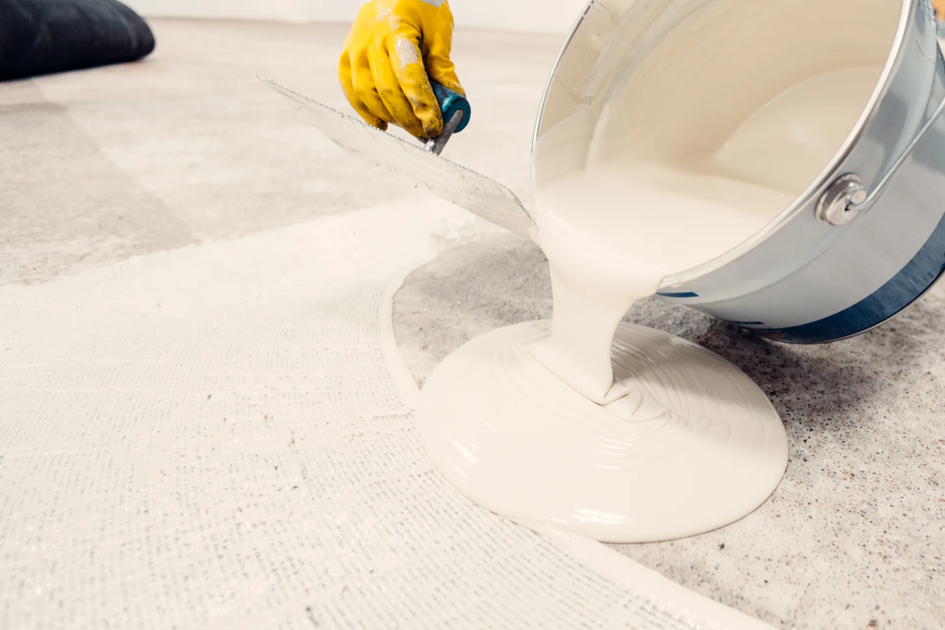 Pail pouring self-leveller out across a primed floor.
