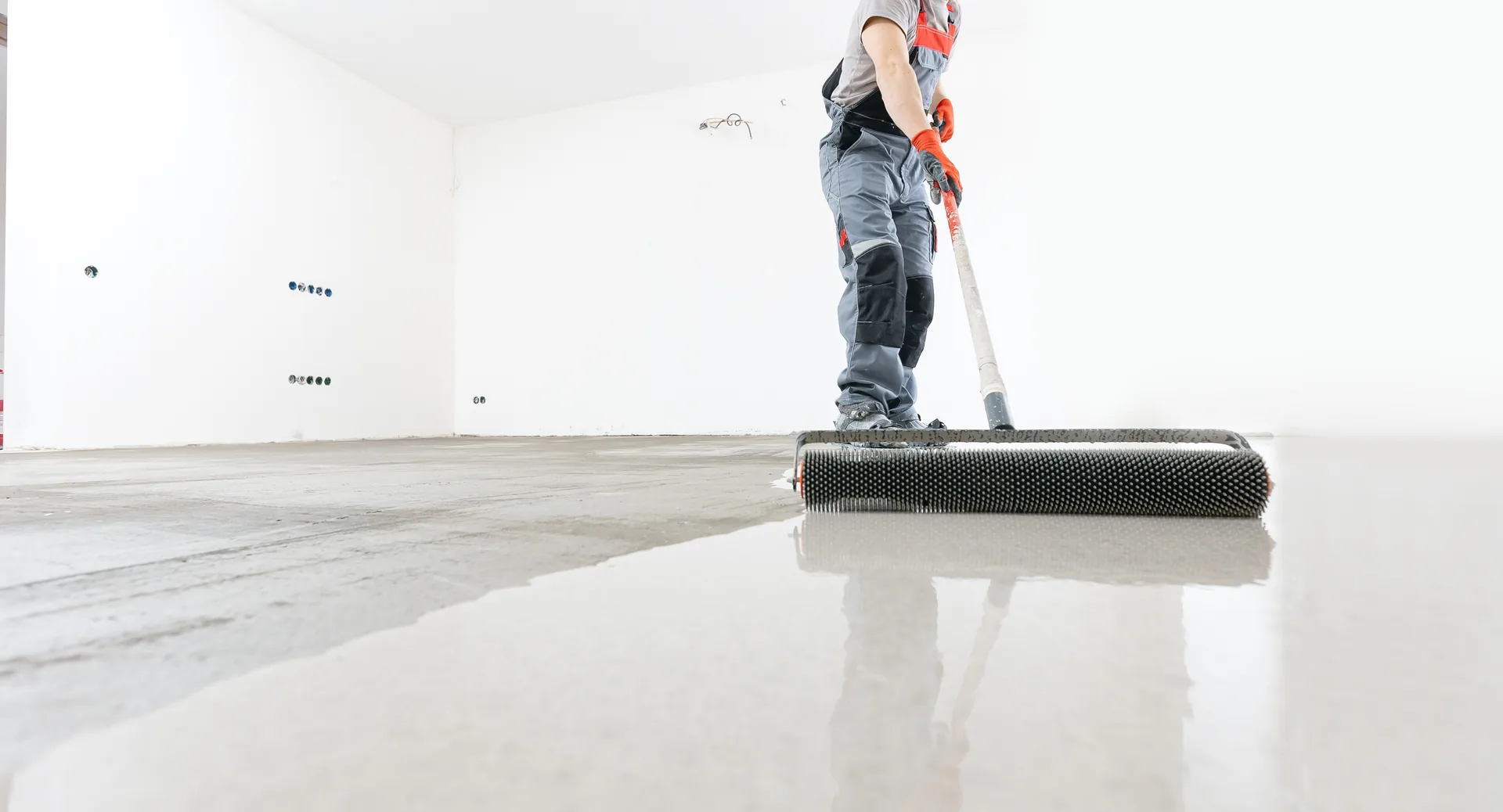Tradesperson pushing a spike roller across freshly poured self-levelling compound.