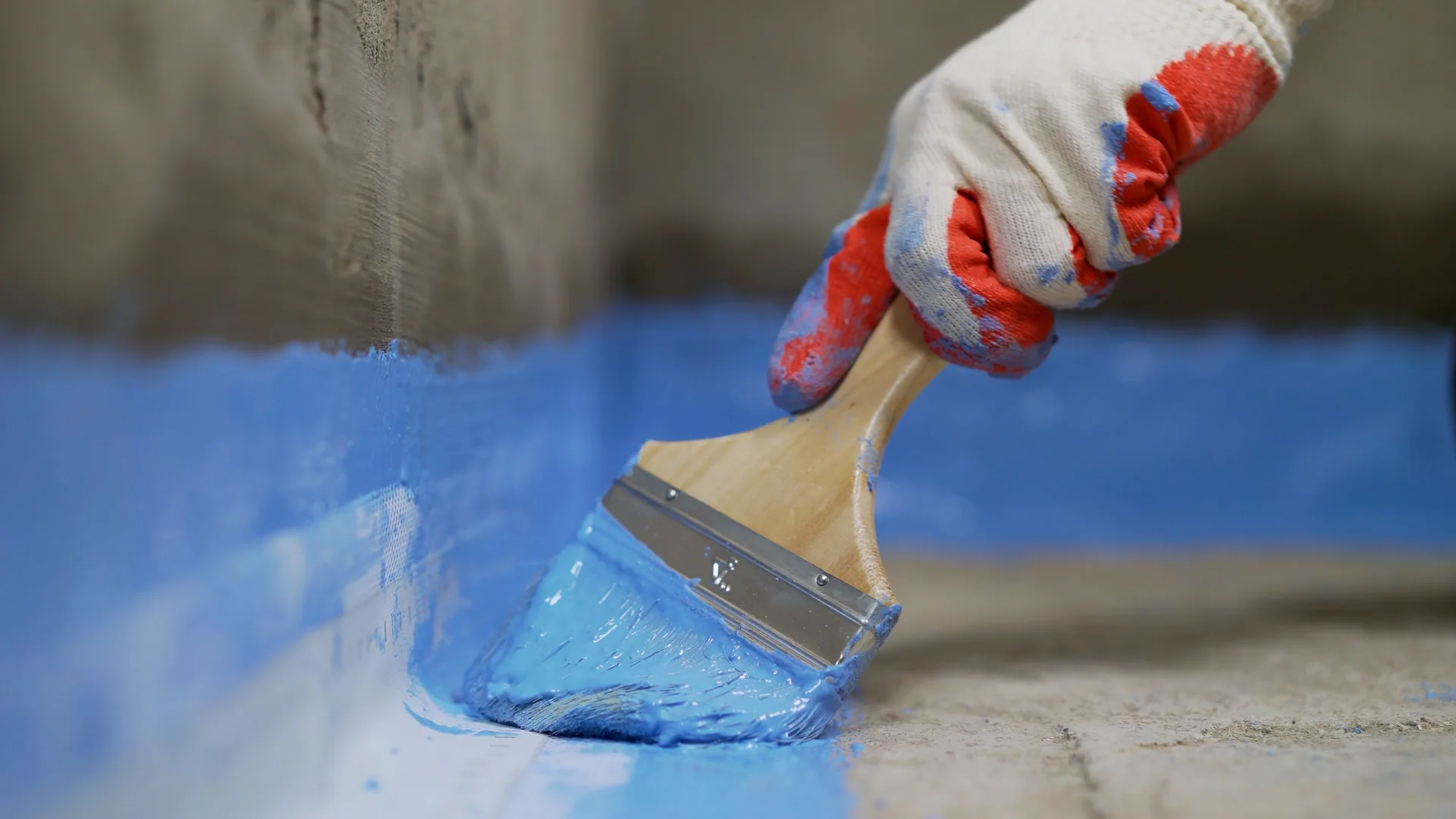 Close-up of a brush applying blue waterproofing membrane.